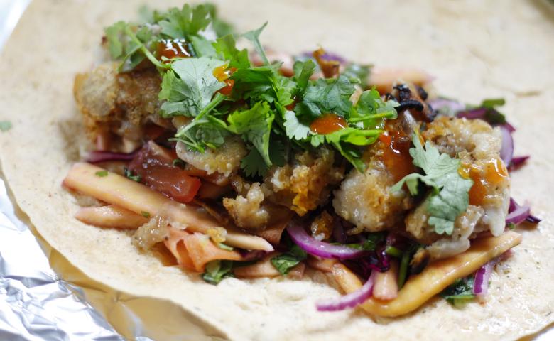 Chicken wrap filled with crispy fried pieces, fresh vegetables, and coriander, drizzled with sauce