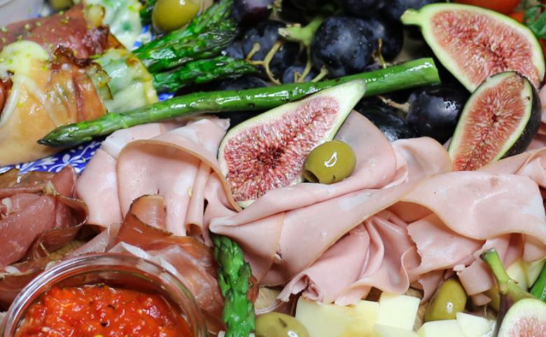 Charcuterie platter with sliced cured meats, figs, asparagus, cheese cubes, olives, and red dip